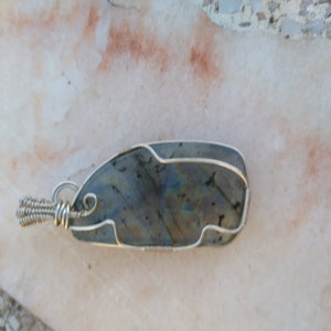 May include: A silver wire wrapped pendant featuring a dark gray labradorite gemstone with iridescent blue and green hues.