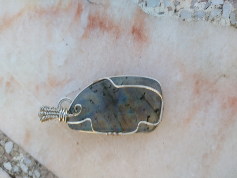 May include: A silver wire wrapped pendant featuring a dark gray labradorite gemstone with iridescent blue and green hues.