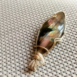 May include: A gold wire wrapped pendant featuring a large iridescent labradorite gemstone. The stone has a unique pattern of blues, greens, and pinks.