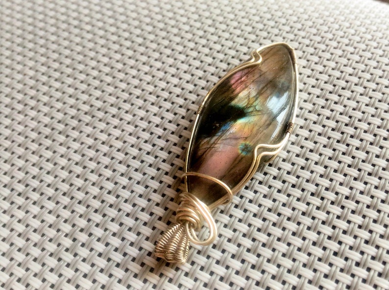 May include: A gold wire wrapped pendant featuring a large iridescent labradorite gemstone. The stone has a unique pattern of blues, greens, and pinks.