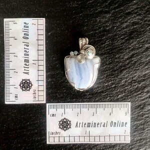 May include: A blue agate pendant wrapped in silver wire with two small clear crystals and a green crystal. The pendant is approximately 2 inches in length.