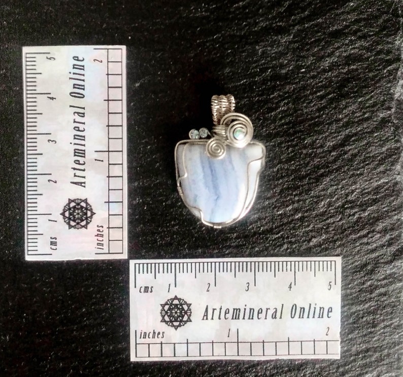 May include: A blue agate pendant wrapped in silver wire with two small clear crystals and a green crystal. The pendant is approximately 2 inches in length.