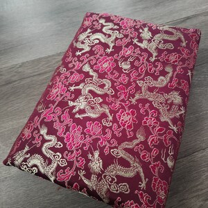 Può includere: Un cuscino color borgogna con un ricamo dorato e rosa di draghi e fiori.