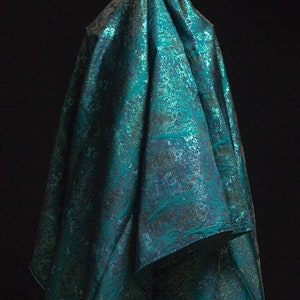May include: A teal blue fabric with a metallic sheen and a subtle pattern. The fabric is draped over a surface.