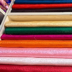 Puede incluir: Un estante con una variedad de telas coloridas, incluyendo rojo, naranja, rosa, blanco, verde y morado. Las telas están dispuestas en filas y todas están dobladas cuidadosamente.