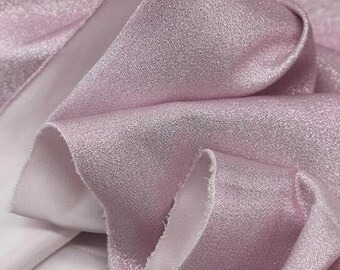 Puede incluir: Primer plano de un trozo de tela rosa claro doblado con una superficie brillante y texturizada. La tela tiene un reverso blanco y está drapeada en pliegues suaves, creando sombras y reflejos.