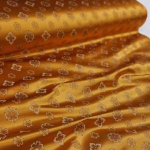 May include: A close-up of a gold fabric with a subtle embossed pattern of small flowers and geometric shapes.