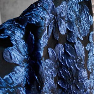 May include: Blue floral fabric with a raised texture. The fabric has a black background with blue flowers that have a 3D effect.