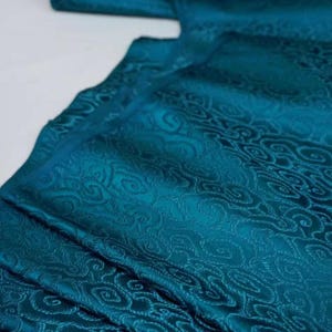 May include: Teal fabric with a raised, swirling pattern. The fabric has a subtle sheen and a soft texture.