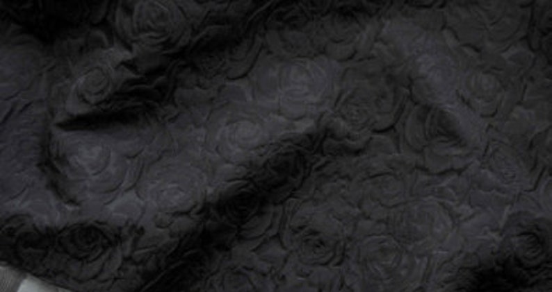 May include: Black fabric with a raised rose pattern. The fabric is textured and has a soft, velvety feel.
