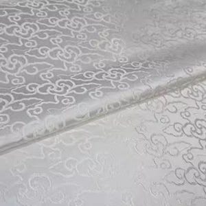 May include: White fabric with a repeating pattern of stylised clouds. The fabric has a subtle sheen and a slightly textured surface.