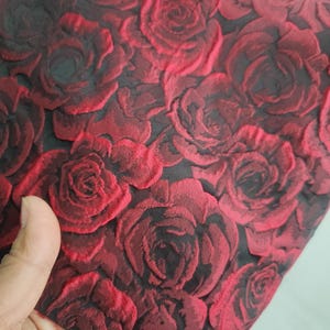 May include: Red fabric with a raised rose pattern. The roses are a dark red and black colour.