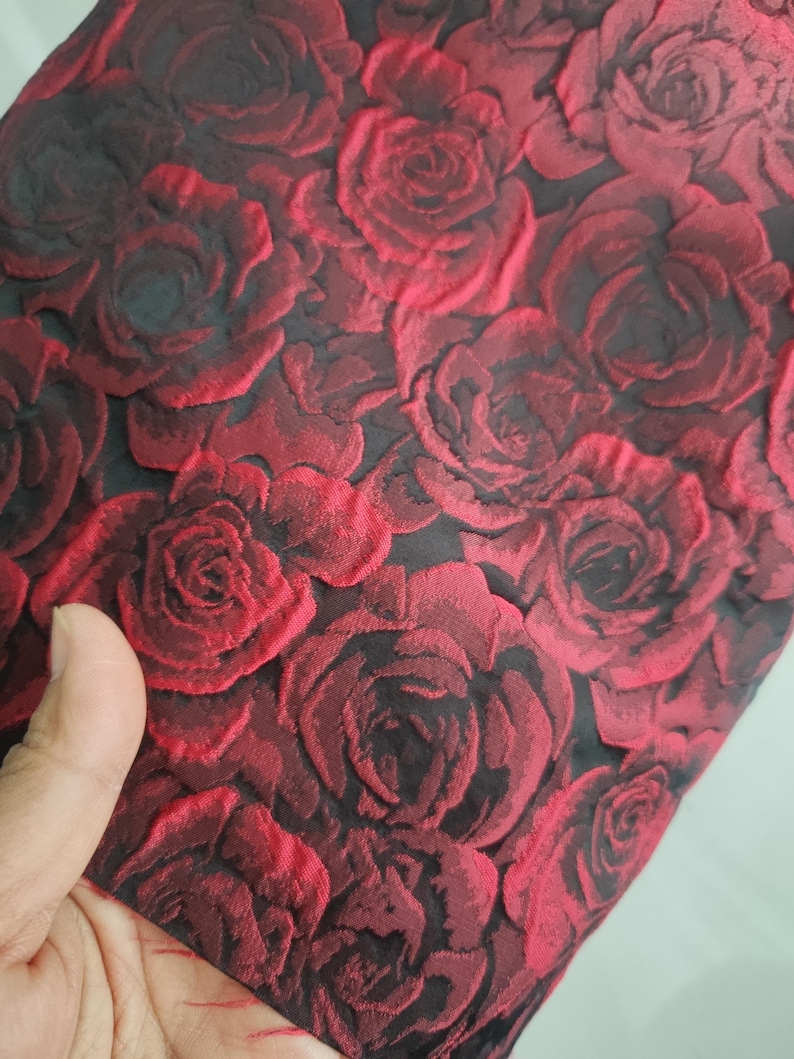 May include: Red fabric with a raised rose pattern. The roses are a dark red and black colour.