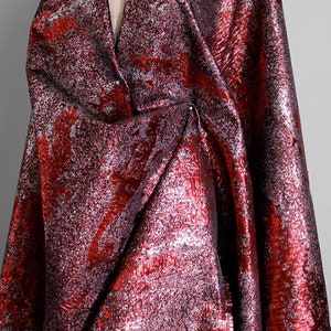 Può includere: Tessuto metallico rosso e argento con un motivo astratto testurizzato. Il tessuto ha un aspetto lucido e leggermente stropicciato.