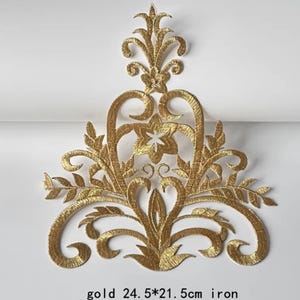 以下が含まれることがあります： 金色の刺繍アップリケ、華やかな花の模様。アップリケのサイズは24.5 x 21.5 cmです。「gold 24.5*21.5cm iron」の文字が下にあります。渦巻き模様、葉、星型の花が特徴です。