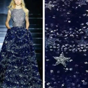 May include: A navy blue tulle fabric with silver glitter and large silver star-shaped sequins. The fabric is sheer and has a delicate texture.