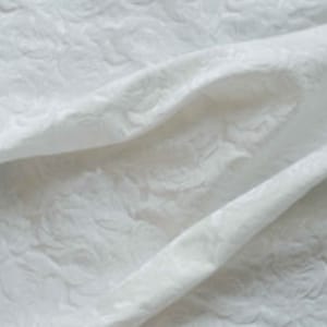 May include: White fabric with a raised floral pattern. The fabric is textured and has a soft, luxurious feel.