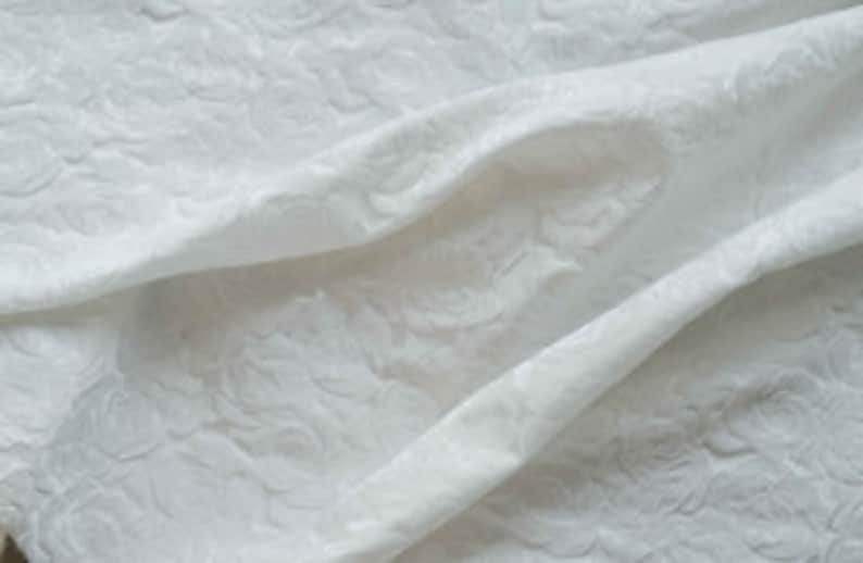 May include: White fabric with a raised floral pattern. The fabric is textured and has a soft, luxurious feel.