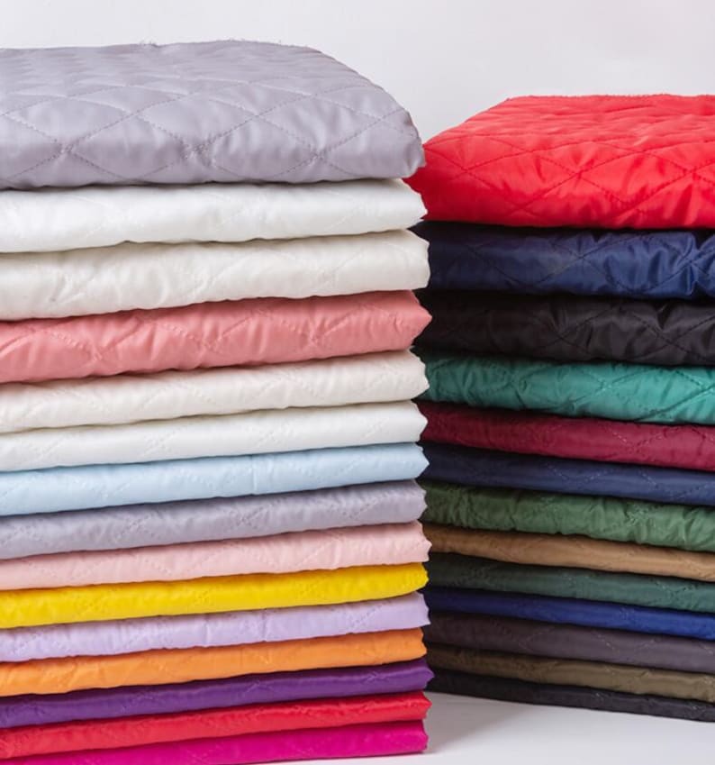 Pode incluir: Uma pilha de tecido acolchoado em v&aacute;rias cores, incluindo branco, rosa, azul, amarelo, laranja, roxo e vermelho. O tecido est&aacute; organizado em uma pilha organizada, com a camada superior de cor cinza claro.