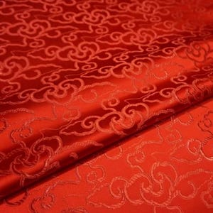 May include: Close-up of red fabric with an embossed cloud pattern. The fabric is folded, showing depth and texture. The color is a vibrant, solid red, with the cloud design slightly darker, creating a subtle contrast.
