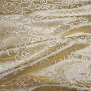 Könnte beinhalten: Nahaufnahme eines cremefarbenen Stoffes mit einem erhabenen Muster aus weißen Wolken. Der Stoff hat einen seidigen Glanz und ist perfekt für Polster oder Kleidung.