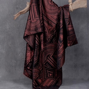 May include: A draped fabric with a geometric pattern in shades of burgundy and black. The fabric is hanging from a wooden branch, showcasing its texture and design. The pattern features curved and angular lines, creating a modern aesthetic.