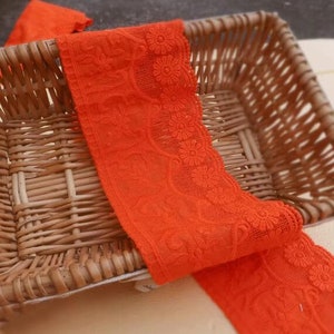 May include: Orange lace trim with a floral design. The lace is in a wicker basket.