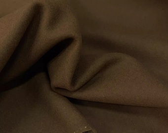 May include: Close-up of a folded piece of brown fabric. The fabric has a soft, textured appearance with visible folds and creases. The color is a rich, earthy brown, and the edges of the fabric are visible.