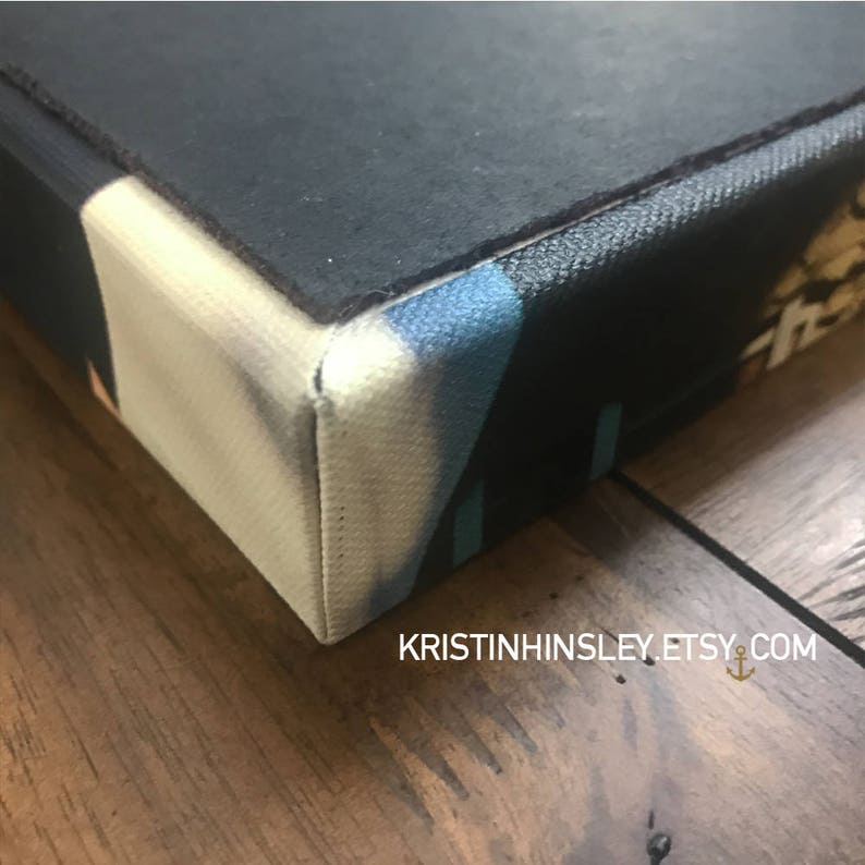 May include: Close-up of the edge of a canvas painting with a black, white, blue, and yellow abstract design. The canvas is wrapped around the edges of the frame.