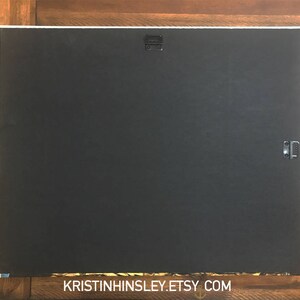 May include: A black canvas print with a white border and two metal hanging clips on the back. The print is blank and ready for a custom design.
