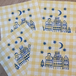 May include: Four yellow and white gingham fabric squares with a blue and white print of a crescent moon, stars, and a cityscape.