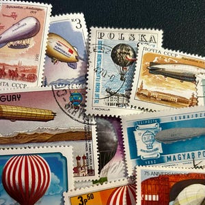 May include: A collection of vintage postage stamps featuring images of airships and hot air balloons. The stamps showcase various designs, colors, and text, including the words "POLSKA" and "CCCP". The stamps are arranged on a dark surface.