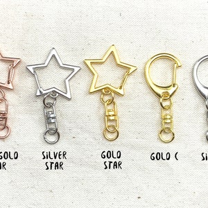 K&ouml;nnte beinhalten: F&uuml;nf Schl&uuml;sselanh&auml;nger mit Stern- und Hakenformen. Die Schl&uuml;sselanh&auml;nger sind in Ros&eacute;gold, Silber und Gold erh&auml;ltlich.