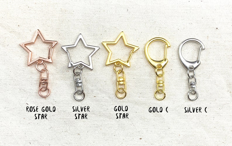 K&ouml;nnte beinhalten: F&uuml;nf Schl&uuml;sselanh&auml;nger mit Stern- und Hakenformen. Die Schl&uuml;sselanh&auml;nger sind in Ros&eacute;gold, Silber und Gold erh&auml;ltlich.