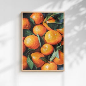 May include: A framed print featuring a still life of oranges. The oranges are a vibrant orange color, with some showing green leaves. The artwork is set against a dark background, creating a contrast that highlights the fruit.