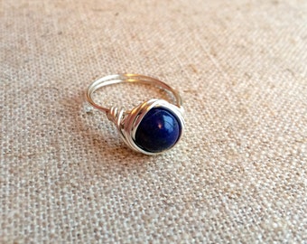 May include: A silver wire wrapped ring with a dark blue gemstone.