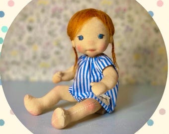 May include: A fabric doll with ginger hair in pigtails, blue eyes, and rosy cheeks, wearing a blue and white striped dress. The text reads: Die Puppenmacherschule, Mini Baby Pippa, Anleitung & Schnittmuster für eine 20cm Babypuppe mit beweglichem Kopf.