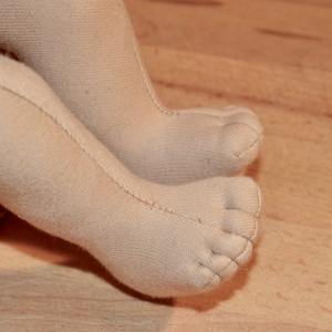 May include: Close-up of a pair of beige knitted tights with a seam down the back of the legs. The toes are sewn shut.