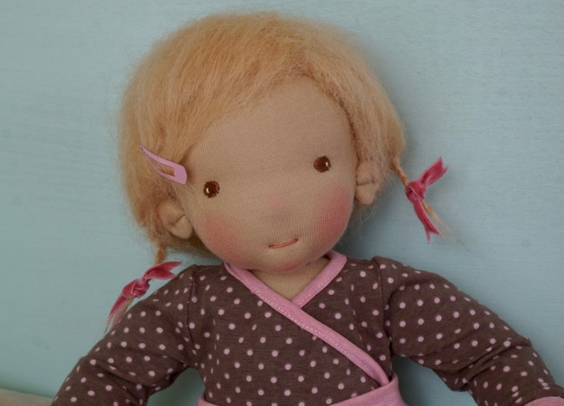 May include: A handmade doll with blonde hair, brown eyes, and rosy cheeks. The doll is wearing a brown and white polka dot dress with a pink trim.