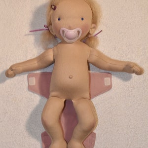 May include: A doll with blonde hair wearing a pink diaper and a pacifier. The doll has blue eyes and a light brown complexion.