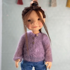 May include: A doll with long brown hair in a bun, wearing a purple knitted sweater and blue jeans.