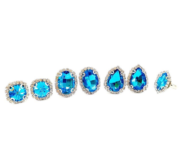 Puede incluir: Una colecci&oacute;n de joyas con piedras preciosas azules, que incluye pendientes y un anillo. Las piedras est&aacute;n engastadas en metal plateado y rodeadas de peque&ntilde;os cristales transparentes. Los pendientes tienen varias formas.