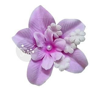 May include: A purple flower with white flowers and a pearl in the centre. The flower is made of fabric and is a decorative element.