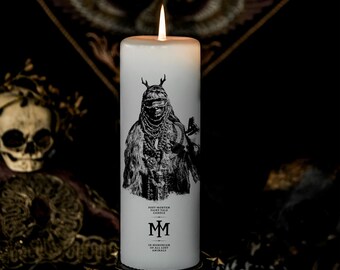 Op de afbeelding: Een brandende witte pilaar kaars met een zwart-wit illustratie van een figuur met geweien en sieraden. De kaars heeft de tekst "Post-Mortem Fairytale Candle" en "In Memoriam of Lost Animals".
