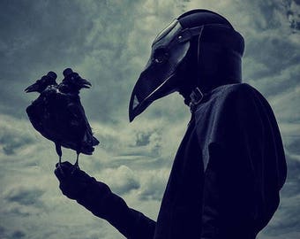 May include: A person wearing a black plague doctor mask and a long black coat holds two black ravens in their gloved hand. The background is a cloudy sky.