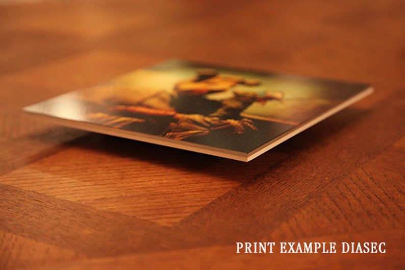 May include: A close-up of a printed photograph mounted on a thick, white, rectangular board. The photograph shows a person in a dynamic pose, with a warm, golden light illuminating the scene.