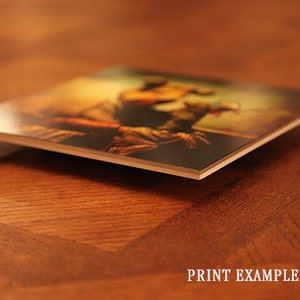 May include: A close-up of a printed photograph mounted on a thick, white, rectangular board. The photograph shows a person in a dynamic pose, with a warm, golden light illuminating the scene.