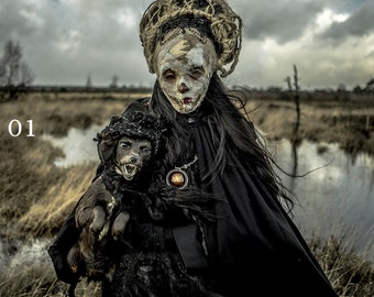 May include: A person in a dark cloak and elaborate headpiece, holding a small dog. The person's face is painted with a skull-like design. The dog wears a matching hat and has bared teeth. The number "01" is in the upper left corner.