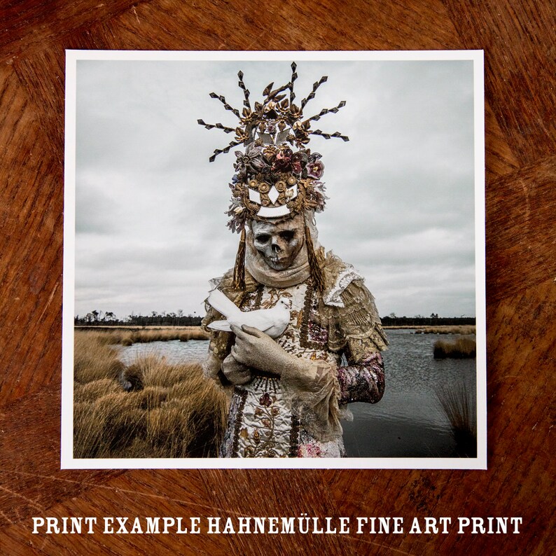 May include: A skeletal figure wearing a gold and white crown with a white dove in their hands. The figure is standing in a marsh with tall grass and water in the background.