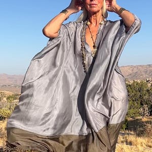 May include: A loose-fitting, flowing kaftan dress featuring a two-tone design with a light grey upper section and a dark olive green hem. The garment has a deep V-neckline, wide sleeves, and a lightweight, semi-sheer fabric that drapes loosely.